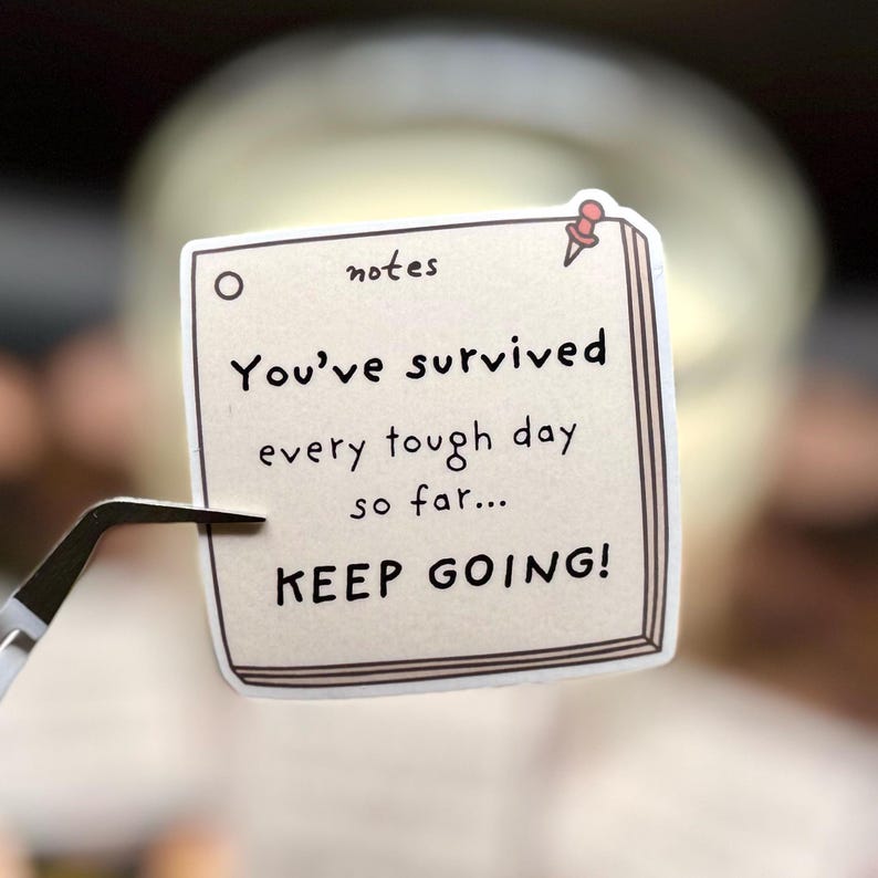 May include: A square sticker designed to look like a notepad page with a light beige background and a brown border. It features a small red pushpin icon and the text: notes, You've survived every tough day so far... KEEP GOING!