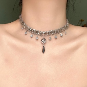 May include: A silver choker necklace with a dangling crystal pendant and smaller crystals along the chain.