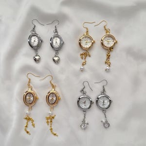 May include: Four pairs of unique earrings featuring miniature watch faces. Two pairs are silver-toned with heart or crystal charms, and two are gold-toned with pearl and chain accents. The watch faces have white dials and black hands.