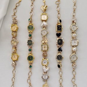 Puede incluir: Cinco pulseras de reloj doradas con varias esferas y dijes decorativos. Las esferas tienen diferentes formas, incluyendo redondas, cuadradas y de corazón. Las pulseras están conectadas por eslabones de cadena dorados.