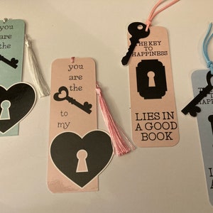 May include: Four pink and blue bookmarks with black keyhole designs and key illustrations. The bookmarks have tassels and the text "You are the key to my..." and "The key to happiness lies in a good book".
