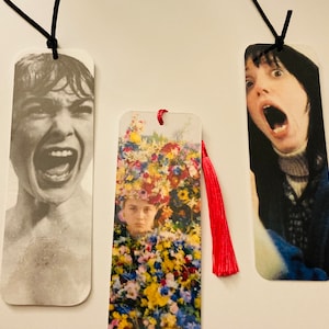 May include: Three bookmarks with different images. The first bookmark features a black and white image of a person with a shocked expression. The second bookmark features a colorful image of a person wearing a flower crown. The third bookmark features a color image of a person with a shocked expression.