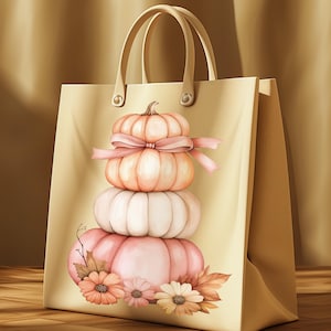 May include: A beige tote bag with a watercolour illustration of stacked pumpkins in pink and peach hues, decorated with a pink bow and flowers. The bag has two handles and is set against a warm, neutral backdrop.