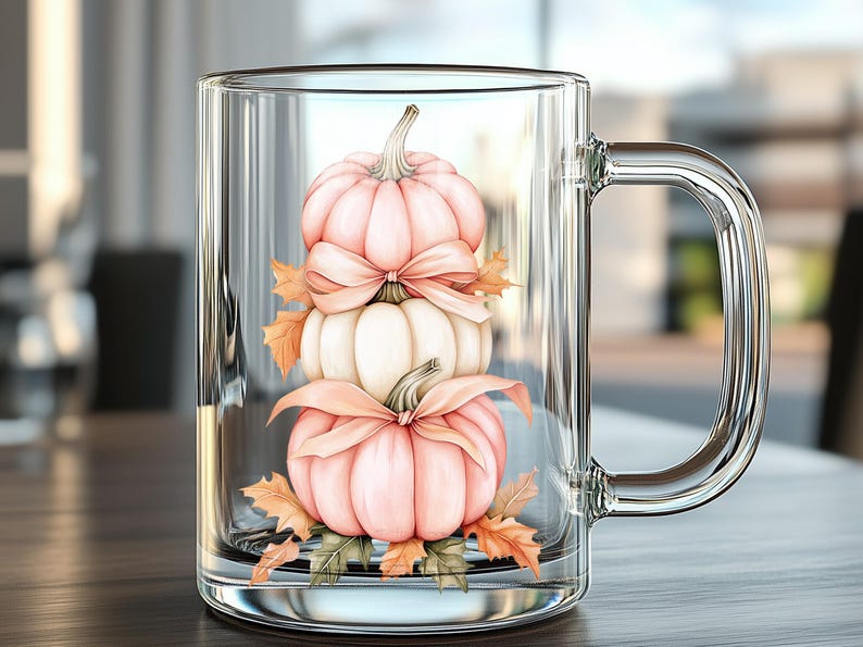May include: A clear glass mug with a handle, featuring a stacked pumpkin design. The pumpkins are in shades of pink and white, adorned with bows and autumn leaves. The mug is set on a wooden surface.