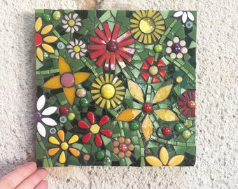 May include: A colorful mosaic wall art featuring a variety of flowers in shades of red, yellow, green, and white. The flowers are arranged in a random pattern, creating a vibrant and eye-catching design.