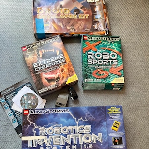 May include: A collection of LEGO Mindstorms robotics kits, including the Robotics Invention System 1.5, Droid Developer Kit, Extreme Creatures Expansion Set, and Robo Sports Expansion Set. The kits feature colorful boxes with images of robots and the LEGO Mindstorms logo.