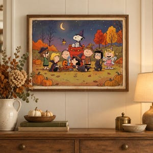 Op de afbeelding: Een ingelijste rechthoekige wandkunstprint met de Peanuts-personages verkleed in Halloween-kostuums in een herfstlandschap met pompoenen, bomen en een maansikkel. Snoopy zit op een rood hondenhok terwijl vrienden zich verzamelen.