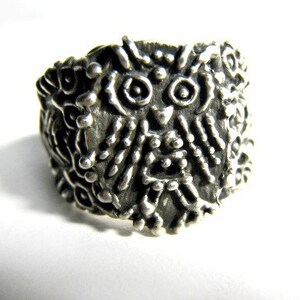 May include: A silver ring with an owl design. The owl's eyes are large and round, and its feathers are detailed.