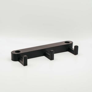 Könnte beinhalten: Ein schwarzer, wandmontierter Schlüsselhalter aus Kunststoff mit drei Haken.