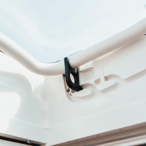 Puede incluir: Primer plano de una barra blanca curvada con un soporte negro. El soporte tiene una abertura circular. El fondo es un cielo azul claro y brillante, lo que sugiere un entorno al aire libre. El tema es arquitectónico o estructural.