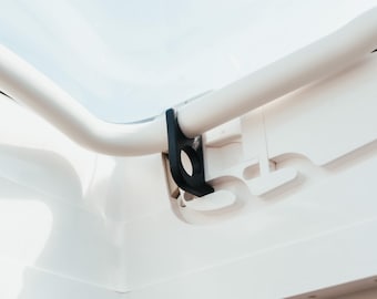 Op de afbeelding: Close-up van een witte, gebogen balk met een zwarte beugel. De beugel heeft een cirkelvormige opening. De achtergrond is een heldere, lichtblauwe lucht, wat een buitenomgeving suggereert. Het thema is architecturaal of structureel.