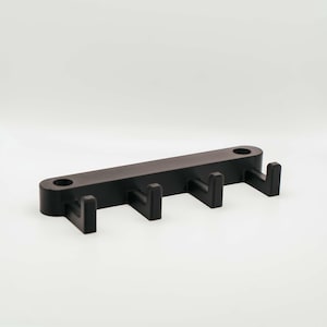 Könnte beinhalten: Ein schwarzer, wandmontierter Hakenhalter aus Kunststoff mit vier Haken.