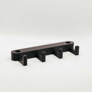 Könnte beinhalten: Ein schwarzer Schlüsselhalter zur Wandmontage mit vier Haken. Das rechteckige Design hat abgerundete Kanten und zwei Löcher zur Befestigung. Die Haken sind gleichmäßig verteilt und zeigen nach unten. Ein einfaches, funktionales Design, ca. 20 cm lang.