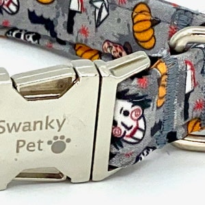 May include: A gray dog collar with a Halloween-themed pattern featuring pumpkins, bats, and a scary face. The collar has a silver metal buckle and a D-ring. The text "Swanky Pet" is printed on the buckle.