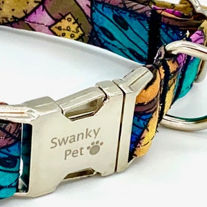 May include: A pet collar featuring a colorful patchwork pattern of blue, purple, and yellow fabric. The collar includes a silver-toned metal side-release buckle engraved with the text Swanky Pet and a paw print icon, along with a silver metal D-ring.