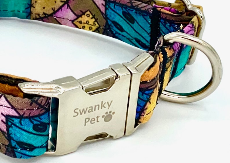 May include: A pet collar featuring a colorful patchwork pattern of blue, purple, and yellow fabric. The collar includes a silver-toned metal side-release buckle engraved with the text Swanky Pet and a paw print icon, along with a silver metal D-ring.
