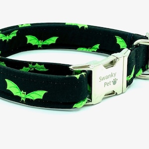 Puede incluir: Collar para perros negro con un patrón repetido de murciélagos verdes. El collar tiene una hebilla de metal plateado y una anilla en D. El texto "Swanky Pet" está impreso en la hebilla.