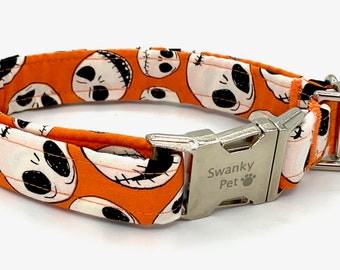 May include: Orange dog collar with a repeating pattern of white skull faces with black details. The collar has a silver metal buckle and a D-ring. The buckle is engraved with "Swanky Pet".