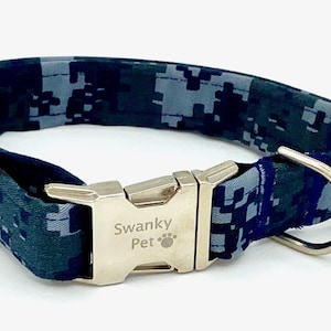 Op de afbeelding: Een huisdierhalsband met een blauw en grijs digitaal camouflagepatroon. De halsband is voorzien van een zilverkleurige metalen gesp met de gravure Swanky Pet en een pootafdruk-icoon, inclusief een zilveren metalen D-ring voor bevestiging.