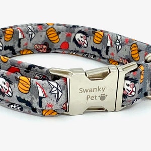 May include: A gray Halloween-themed dog collar with a repeating pattern of pumpkins, bats, knives, and a scary face. The collar has a silver metal buckle and a D-ring. The text "Swanky Pet" is printed on the buckle.
