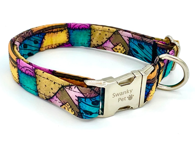 May include: A pet collar featuring a patchwork pattern of teal, purple, and tan fabric squares with black stitched details. The collar includes a silver-toned metal side-release buckle engraved with the text Swanky Pet and a paw print icon.
