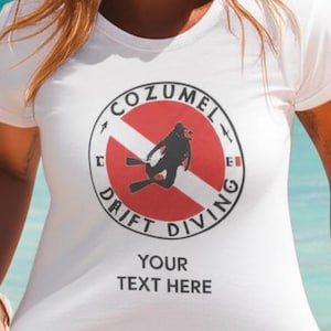 Puede incluir: Camiseta blanca con un diseño gráfico redondo que presenta la silueta de un buceador dentro de un círculo rojo y blanco, con el texto "COZUMEL DRIFT DIVING" y "YOUR TEXT HERE". La camiseta es de manga corta.