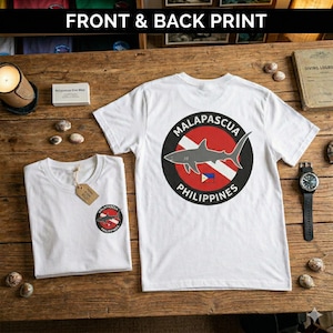Puede incluir: Dos camisetas blancas, una doblada y otra desplegada, con un diseño gráfico circular que presenta un tiburón, el texto "MALAPASCUA" y "PHILIPPINES". El texto "FRONT & BACK PRINT" está en la parte superior de la imagen.