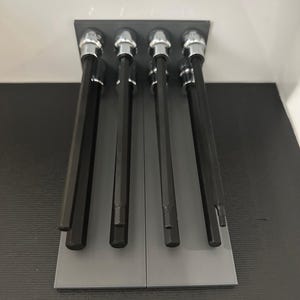 May include: A set of six black hex key wrenches with silver tops, neatly arranged in a gray holder. The tools are displayed against a white and black background, showcasing their design and functionality. The wrenches are of varying lengths.