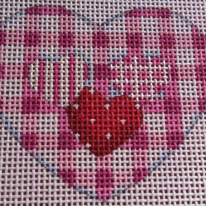 May include: A close-up of a pink and red heart-shaped cross-stitch pattern on white Aida cloth. The heart is outlined in blue and has a smaller red heart in the center.