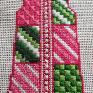 May include: A pink and green cross-stitch embroidery design with a white border. The design features a variety of stitches, including a herringbone stitch, a satin stitch, and a cross stitch.