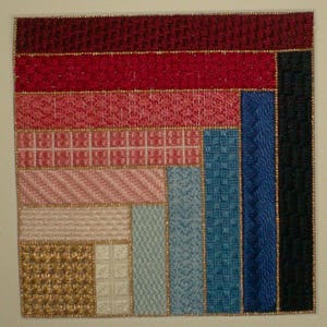 Op de afbeelding: Een kleurrijk geborduurd wandkleed met een geometrisch patroon. Het ontwerp bevat een verscheidenheid aan kleuren, waaronder rood, roze, blauw en goud. De stof is textuurrijk en heeft een handgestikte uitstraling.