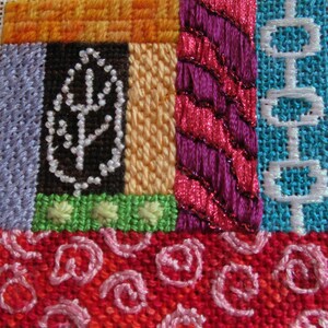 Peut inclure: Un gros plan sur un échantillon de point de croix coloré avec différents motifs et textures. L'échantillon présente un motif de feuille, un motif rayé, un motif géométrique et un motif floral. Les couleurs incluent l'orange, le violet, le vert, le bleu et le rouge.