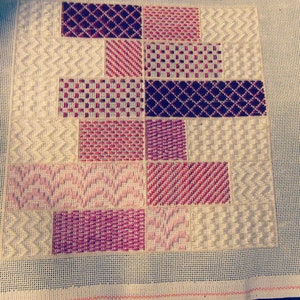 May include: A close-up of a needlepoint canvas featuring a range of stitches in pink, red, and white. The stitches are arranged in a grid pattern, forming a geometric design.