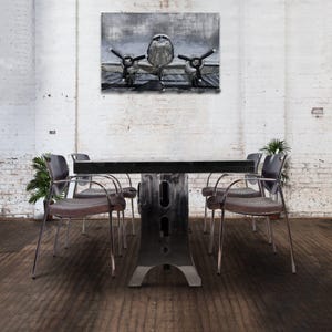 May include: A black metal table with a rectangular top and a unique industrial design. Four chairs with metal frames and gray fabric seats surround the table. A vintage airplane print hangs on the wall behind the table.