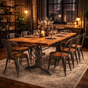 May include: A rectangular wooden dining table with a dark metal industrial base featuring a hand crank mechanism, surrounded by six metal chairs with wooden seats. The table is set with glassware, a vase of dried flowers, and a lit candle.