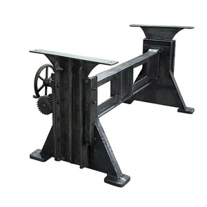 May include: A dark gray, industrial-style table base. The base features a gear mechanism on one end and a rectangular frame with a support structure. The base is made of heavy-duty metal and is designed to support a tabletop. The overall design is sturdy and functional.