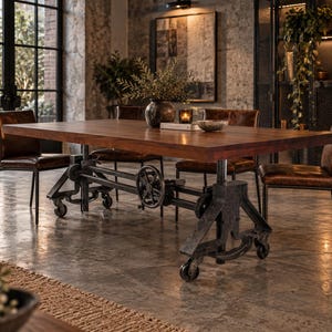 May include: A rectangular wooden dining table with a thick brown top and a dark gray metal base featuring an industrial gear and crank mechanism with wheels. Four brown leather chairs with thin metal legs are positioned around the table.