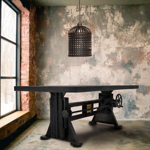 May include: A black industrial-style table with a crank and wheel mechanism. The table is set in a room with a large window, exposed brick, and a hanging metal cage light fixture. A potted plant sits nearby.