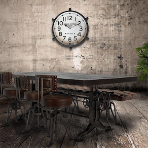 May include: An industrial-style dining table with a dark wood top and metal base, complemented by matching chairs. A large clock with the text "Grand Central Station New York" hangs on the wall. Potted plants flank the table.