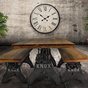 May include: A rustic dining table and benches with a distressed metal base and wooden tabletop. A large clock hangs on the wall above the table. Potted plants flank the table, creating a vintage industrial aesthetic.