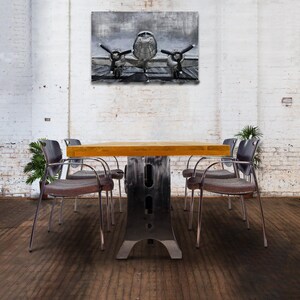 May include: A wooden table with a metal base and six chairs. The table is surrounded by chairs with metal frames and gray cushions. A black and white painting of an airplane hangs on the wall behind the table.