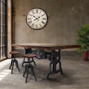May include: A rustic dining table with a dark wood top and industrial-style metal base. Two matching adjustable stools with wooden seats are in front of the table. A large clock with Roman numerals hangs on the wall. A potted plant is to the right.