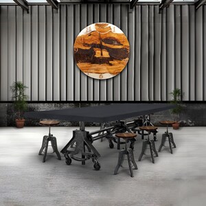May include: A large, black rectangular table with a metal base and wheels, surrounded by several small, round wooden stools with metal legs. A large, round wooden clock hangs on the wall above the table.