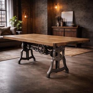May include: A rectangular dining table with a thick, natural-toned wooden top and a heavy-duty, dark gray cast iron base. The base features an intricate mechanical design with visible gears, cogs, and a central hand-crank wheel for height adjustment.