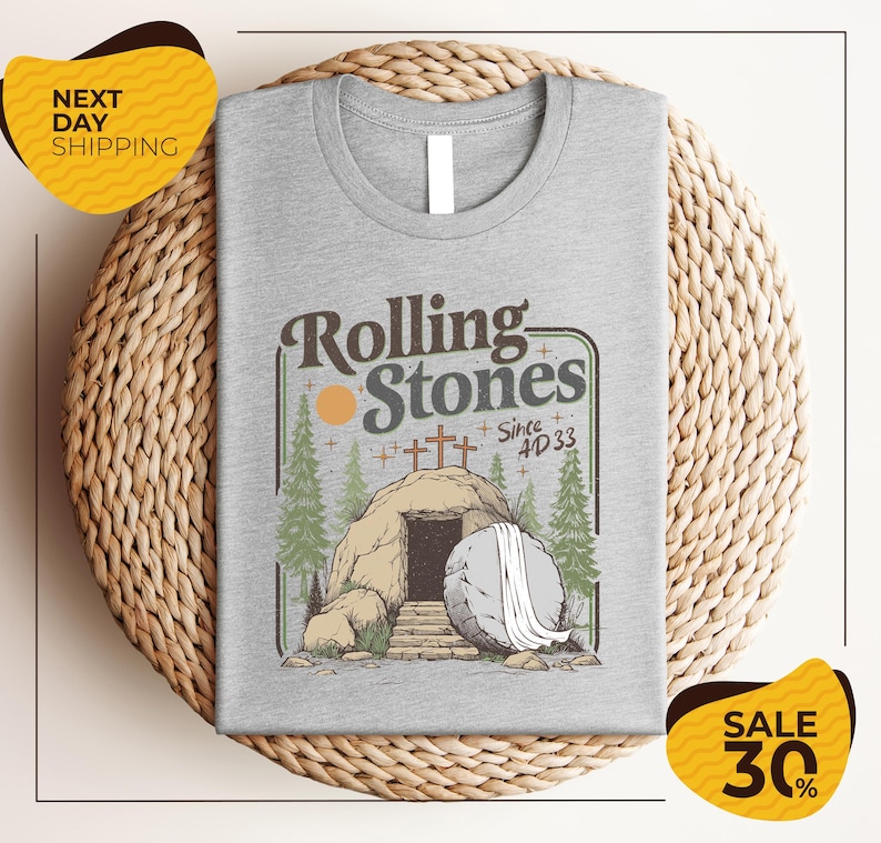 a gray t-shirt with a graphic design depicting a rock with an entrance to an underground passage, surrounded by trees and a cross. The text on the t-shirt reads "Rolling Stones Since 4D33" and there are two yellow sale signs in the image, one on the left and one on the right, indicating a 30% discount on the t-shirt.