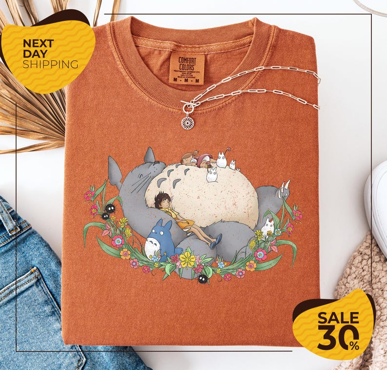 a red t-shirt with a cartoon illustration of a cat and various other characters, such as a blue bird and a gray cat, surrounded by flowers and leaves. The t-shirt is displayed on a white background, and there are yellow and black sale signs indicating a 30% discount.