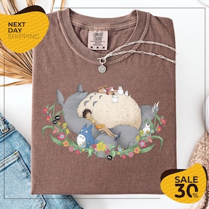 a brown t-shirt with a graphic design depicting a cat surrounded by various cartoon-style animals and flowers. The t-shirt is displayed on a white background, and there are yellow and black sale signs indicating a 30% discount.