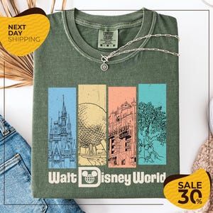 a green t-shirt with a graphic design of Disney World landmarks, including a castle, roller coaster, and other iconic structures. The t-shirt is displayed on a white background, and there are two yellow sale tags visible, one on the left and one on the right, indicating a 30% discount on the item.