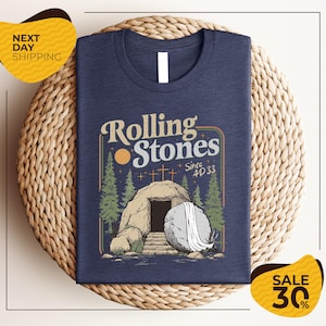 a blue t-shirt with a graphic design depicting a tomb or tombstone, surrounded by trees and a cross, along with the text "Rolling Stones Since #33". The t-shirt is displayed on a woven basket, and there are two yellow price tags in the image, one for "SALE 30%" and another for "NEXT DAY SHIPPING".