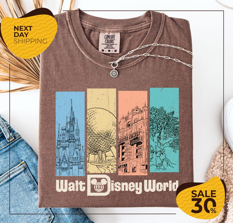 a brown t-shirt with a graphic design of Disney World landmarks, including a castle, roller coaster, and other iconic structures. The t-shirt is displayed on a white background, and there are two yellow sale signs indicating a 30% discount on the item.